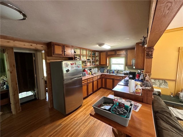 kitchen with light wood-style floors, a textured ceiling, brown cabinetry, freestanding refrigerator, and glass insert cabinets