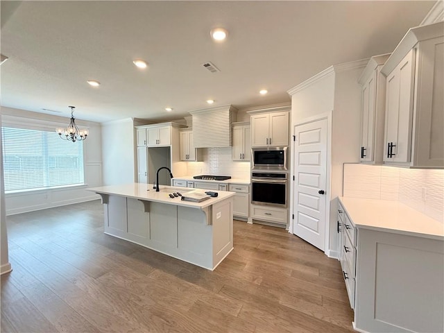 kitchen with light wood-type flooring, a chandelier, tasteful backsplash, a sink, and stainless steel appliances