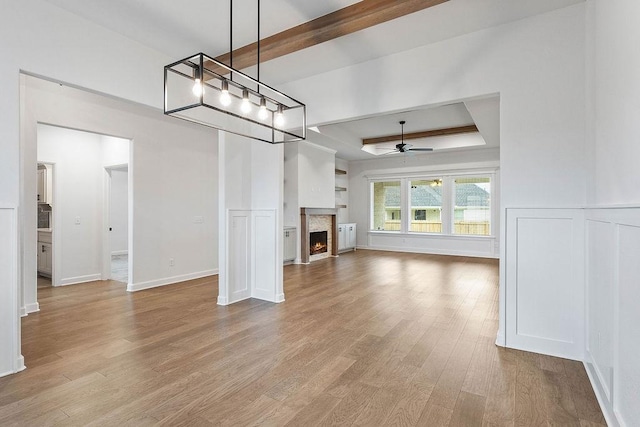 909 Budrio Ave, Tontitown, AR 72762 - unfurnished living room featuring a raised ceiling, light wood finished floors, ceiling fan, a fireplace with flush hearth, and baseboards