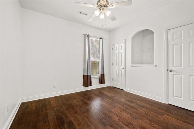spare room with dark wood-style flooring, ceiling fan, visible vents, and baseboards
