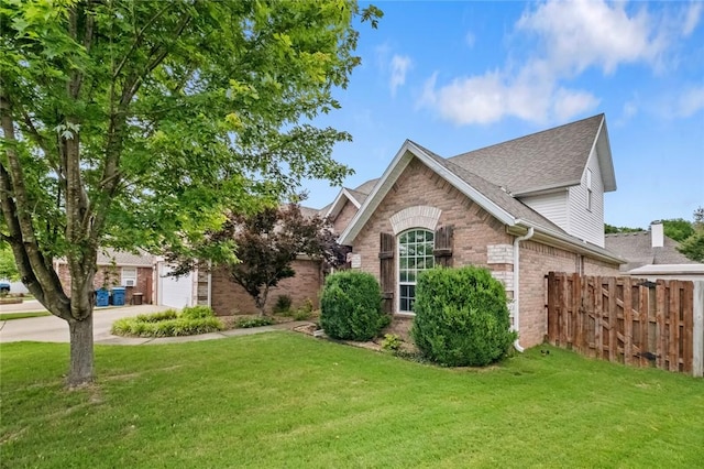 view of front of property featuring a front yard, a garage, brick siding, fence, and a shingled roof