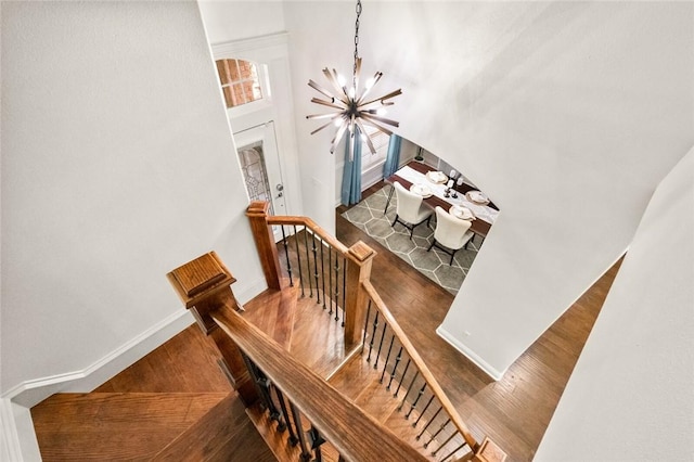 stairway featuring baseboards, wood finished floors, and a notable chandelier