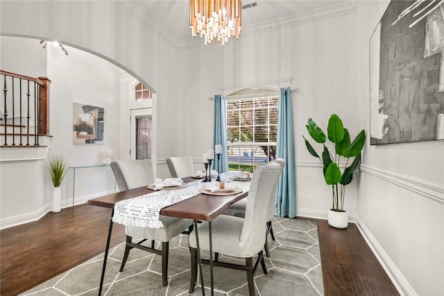 dining area with crown molding, arched walkways, a notable chandelier, and wood finished floors
