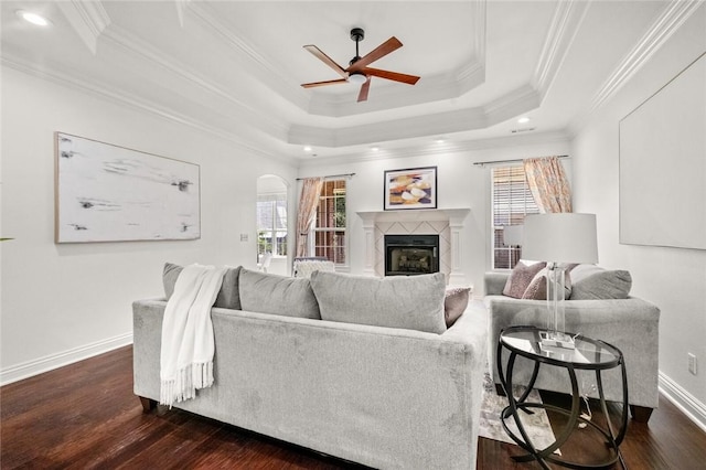 living area with a glass covered fireplace, ceiling fan, a tray ceiling, and dark wood-style floors