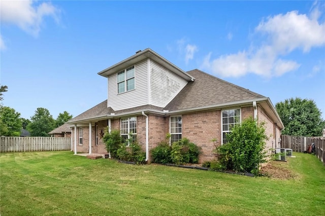 rear view of property with a yard, brick siding, a shingled roof, and a fenced backyard