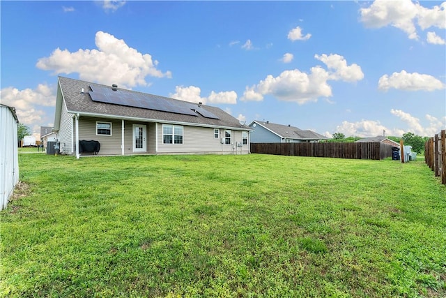 rear view of house with a fenced backyard, a shingled roof, a lawn, central air condition unit, and solar panels