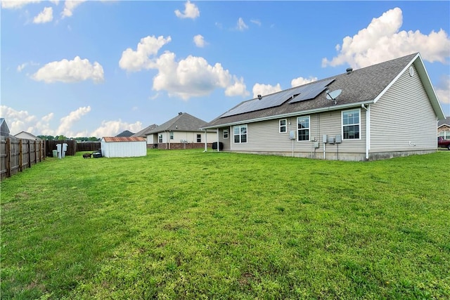 rear view of house featuring an outdoor structure, a fenced backyard, roof mounted solar panels, a lawn, and a storage shed