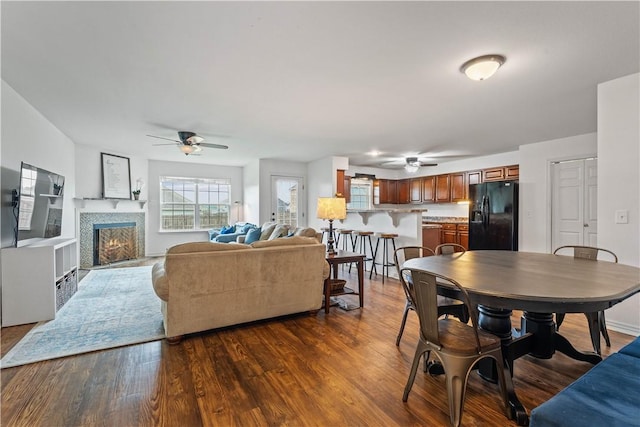dining area with a ceiling fan, a fireplace with flush hearth, and dark wood-style floors