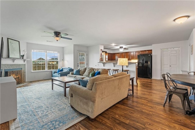 living area with a tiled fireplace, ceiling fan, and dark wood finished floors