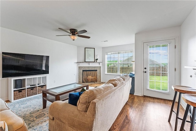 living area featuring a ceiling fan, dark wood-style floors, and a tiled fireplace