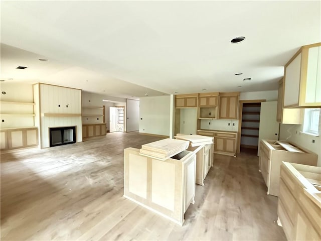 kitchen featuring light brown cabinets, a fireplace, a kitchen island, and light wood-style flooring