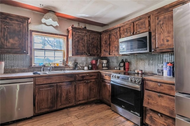 kitchen featuring dark brown cabinetry, appliances with stainless steel finishes, a sink, light wood-style flooring, and backsplash