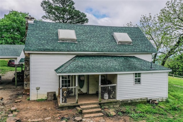 back of property with covered porch, a shingled roof, and a chimney