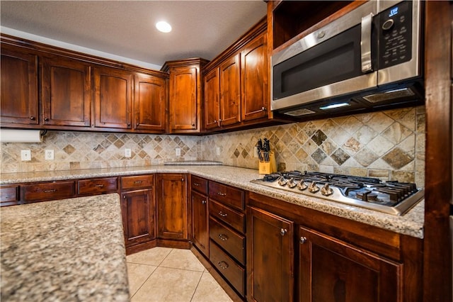 kitchen with light tile patterned flooring, appliances with stainless steel finishes, light stone counters, and tasteful backsplash