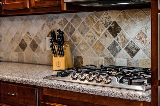 interior details featuring stainless steel gas cooktop, backsplash, range hood, and light countertops