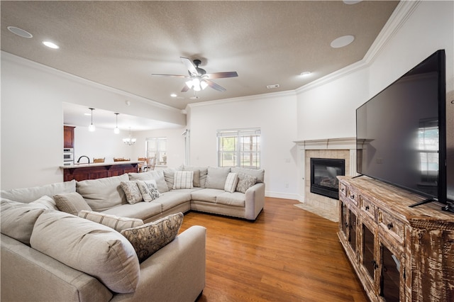 living room featuring ornamental molding, wood finished floors, recessed lighting, a tile fireplace, and ceiling fan with notable chandelier