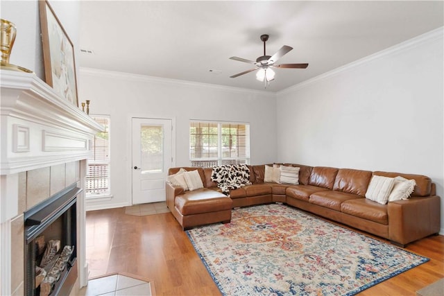 living room featuring ceiling fan, visible vents, crown molding, a tiled fireplace, and wood finished floors