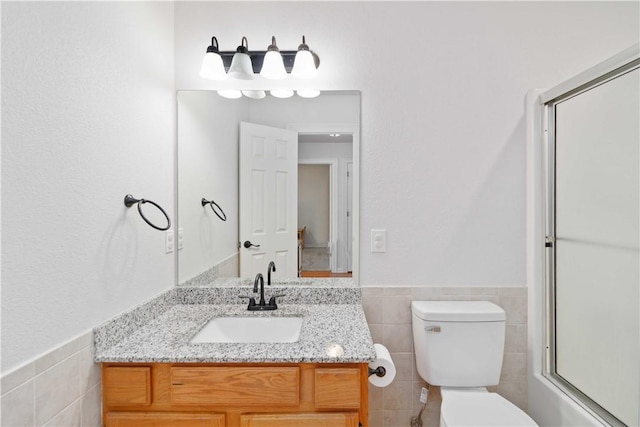 bathroom featuring toilet, tile walls, wainscoting, and vanity