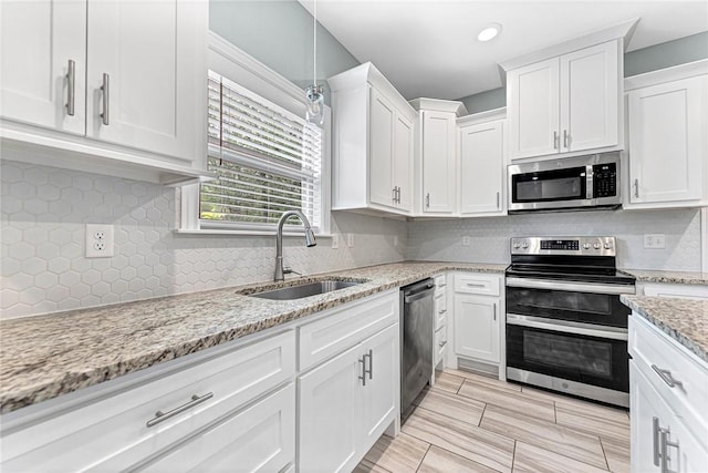 kitchen with decorative backsplash, a sink, light stone counters, white cabinets, and stainless steel appliances