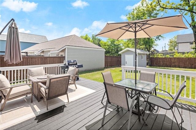 wooden deck featuring a fenced backyard, a storage unit, a lawn, an outbuilding, and outdoor dining space