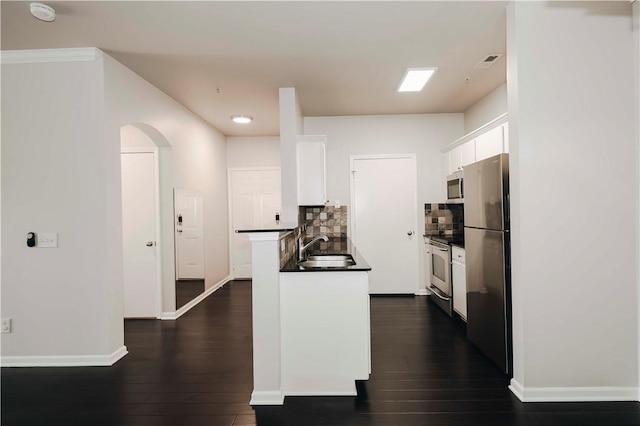 kitchen with white cabinets, dark countertops, a sink, arched walkways, and stainless steel appliances