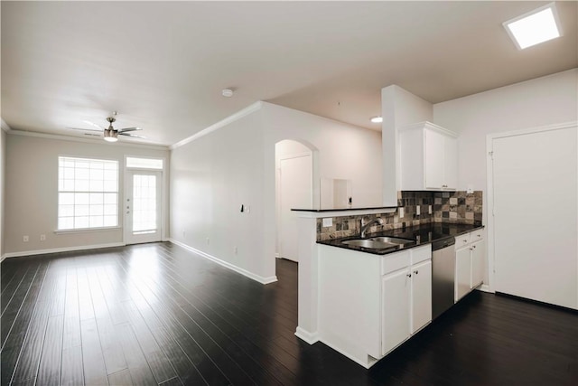 kitchen with a ceiling fan, dark countertops, stainless steel dishwasher, a sink, and a peninsula