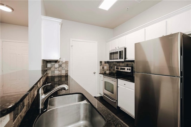 kitchen with white cabinets, appliances with stainless steel finishes, a sink, dark stone counters, and decorative backsplash