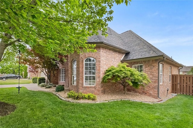 view of home's exterior featuring fence, a shingled roof, a yard, and brick siding