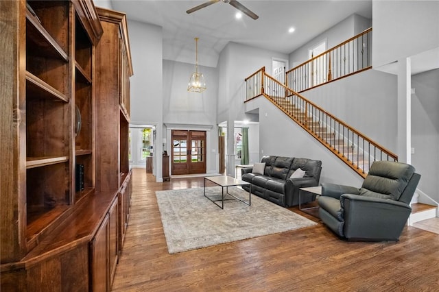 living area featuring ceiling fan with notable chandelier, recessed lighting, wood finished floors, a towering ceiling, and stairway