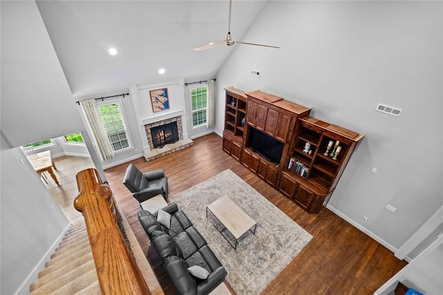 living area with a ceiling fan, visible vents, a fireplace, wood finished floors, and high vaulted ceiling