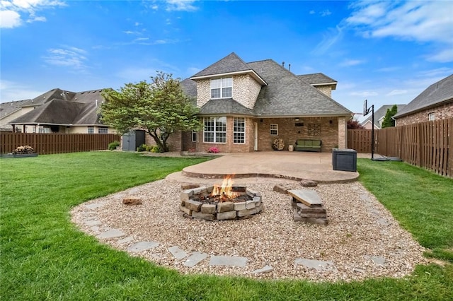 rear view of house featuring brick siding, a fenced backyard, a patio, a yard, and a fire pit