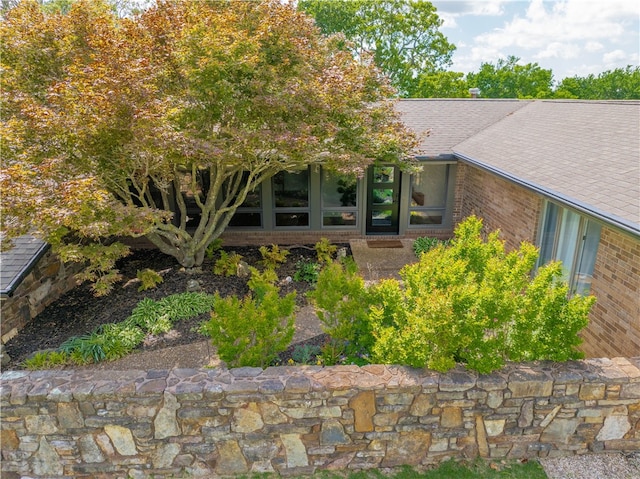 entrance to property with roof with shingles and brick siding