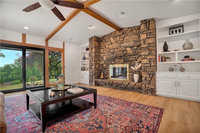 living area with a ceiling fan, a fireplace, lofted ceiling with beams, light wood-style floors, and built in shelves