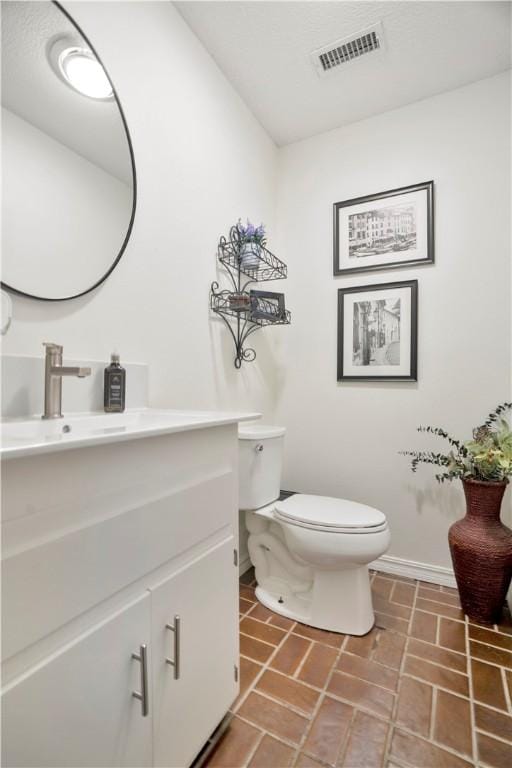 bathroom featuring brick floor, toilet, baseboards, visible vents, and vanity
