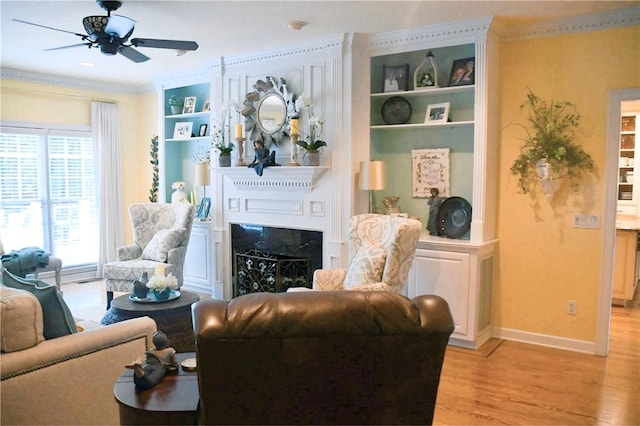 living area featuring light wood-type flooring, crown molding, a fireplace, and ceiling fan