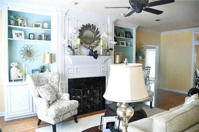 sitting room with ornamental molding, wood finished floors, baseboards, ceiling fan, and a premium fireplace