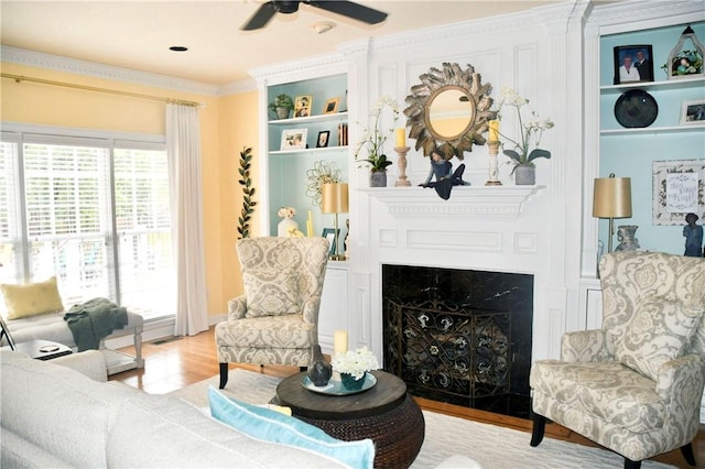 living room with ornamental molding, wood finished floors, a fireplace, ceiling fan, and built in shelves