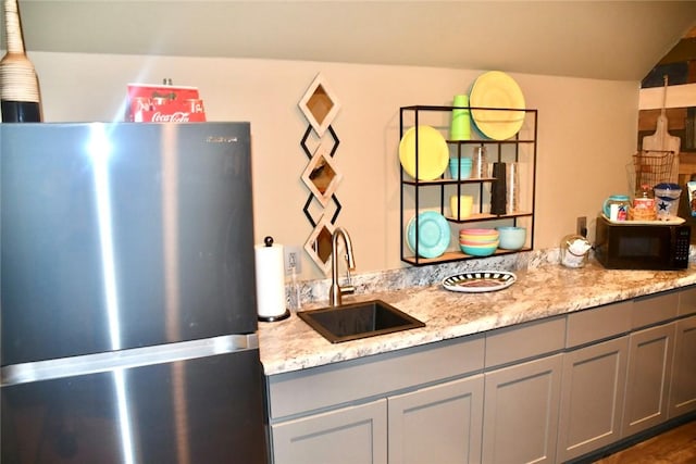 kitchen featuring freestanding refrigerator, a sink, black microwave, and gray cabinetry