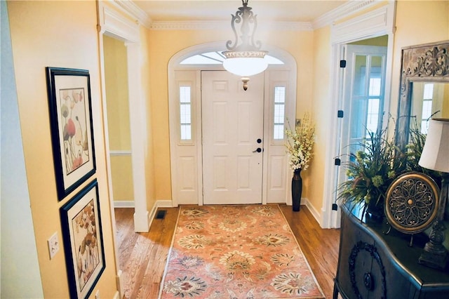 foyer with crown molding, baseboards, light wood-type flooring, and visible vents