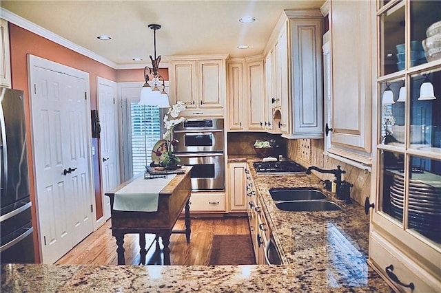 kitchen featuring ornamental molding, light stone countertops, a sink, light wood finished floors, and appliances with stainless steel finishes
