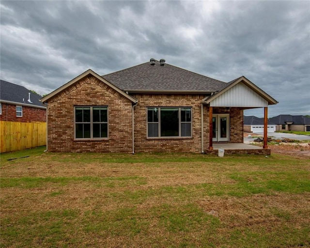 rear view of property featuring fence, brick siding, a shingled roof, a patio area, and a lawn