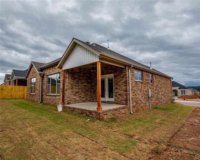 rear view of property featuring a lawn, fence, brick siding, and a patio