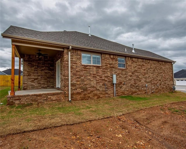 back of house featuring fence, roof with shingles, brick siding, ceiling fan, and a patio