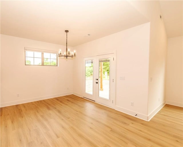 spare room featuring light wood-style floors, baseboards, and a chandelier