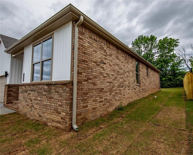 view of side of home featuring a lawn, a garage, fence, and brick siding