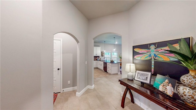 hallway featuring baseboards, arched walkways, high vaulted ceiling, and a sink