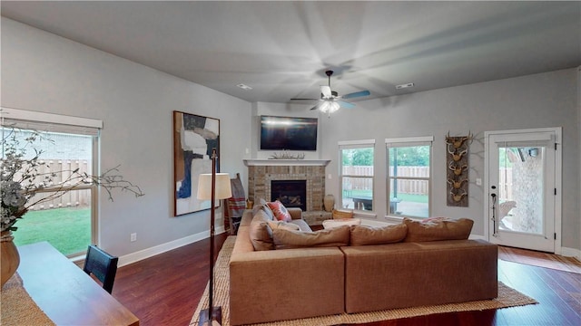 living area featuring baseboards, ceiling fan, a fireplace, and dark wood finished floors