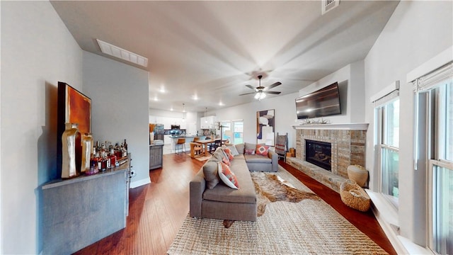 living area with visible vents, a ceiling fan, dark wood finished floors, and a glass covered fireplace