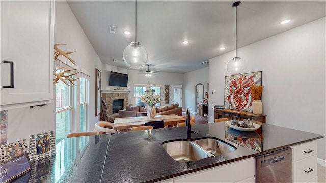 kitchen featuring pendant lighting, a sink, a glass covered fireplace, white cabinets, and a ceiling fan