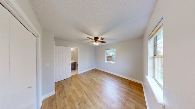 unfurnished bedroom with a closet, baseboards, light wood-type flooring, a textured ceiling, and a ceiling fan